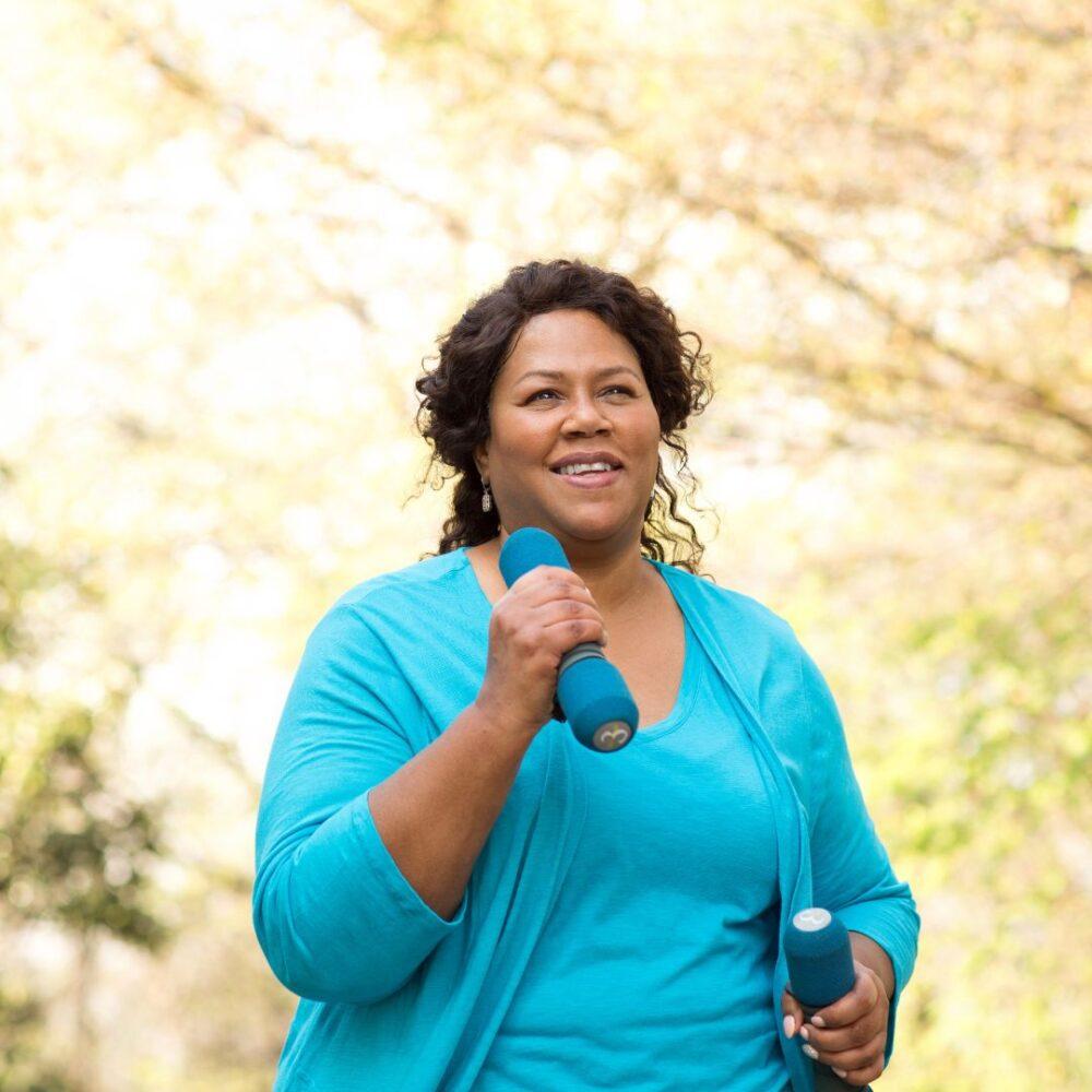 Smiling senior woman walking in woods with hand weights