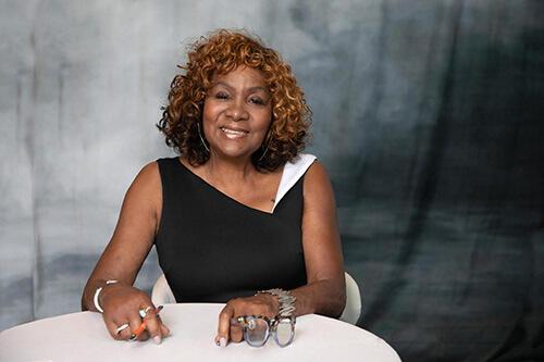 Photo of Leigh Battle sitting at desk wearing professional dress and holding her glasses and a pen