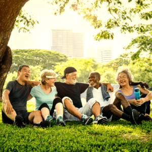 Group of senior friends sitting in the grass in the park, smiling and laughing.