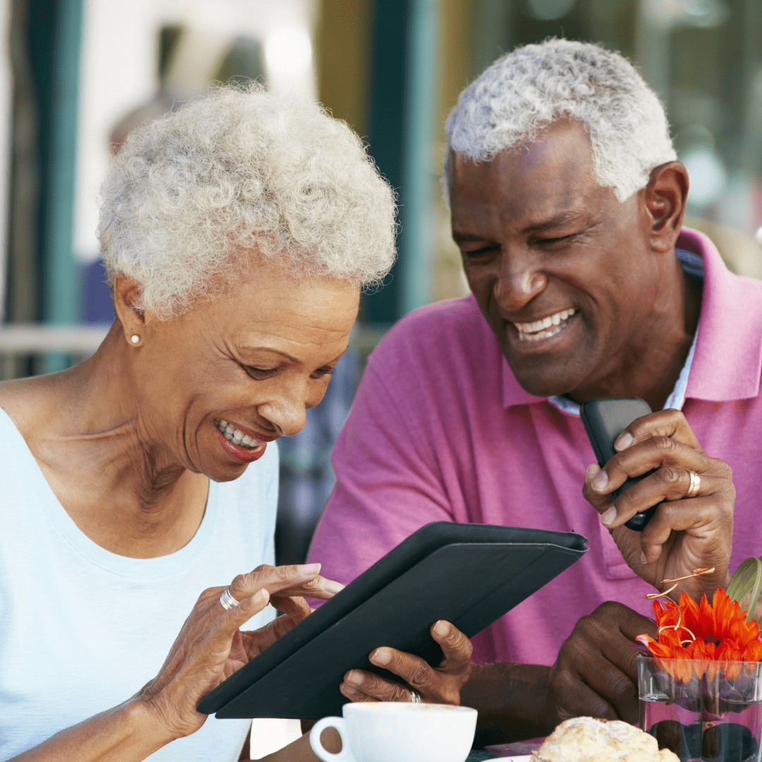Senior man and woman enjoying a cup of coffee while smiling and looking at a tablet together.