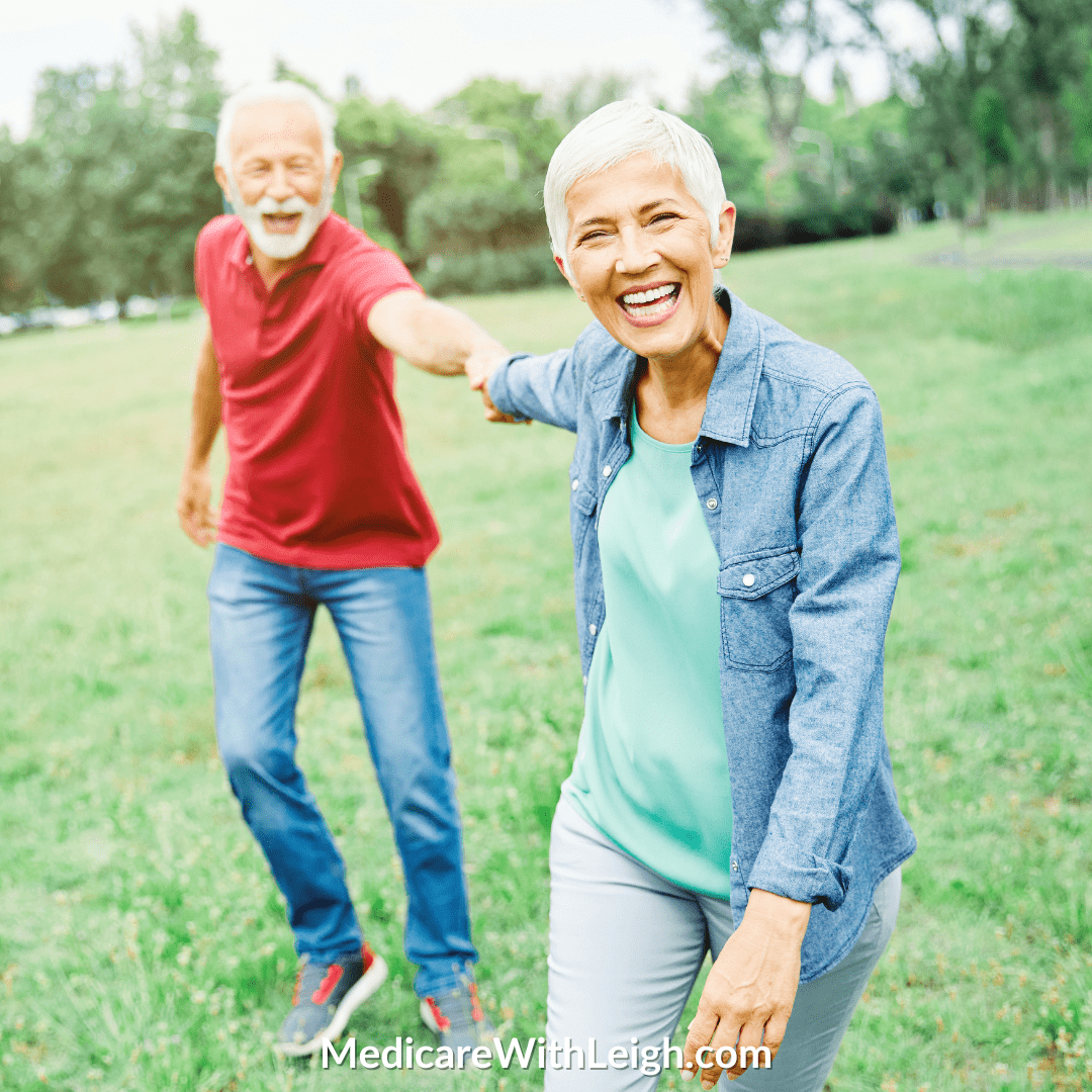 Photo of a senior man and woman smiling and holding hands in a grassy field.