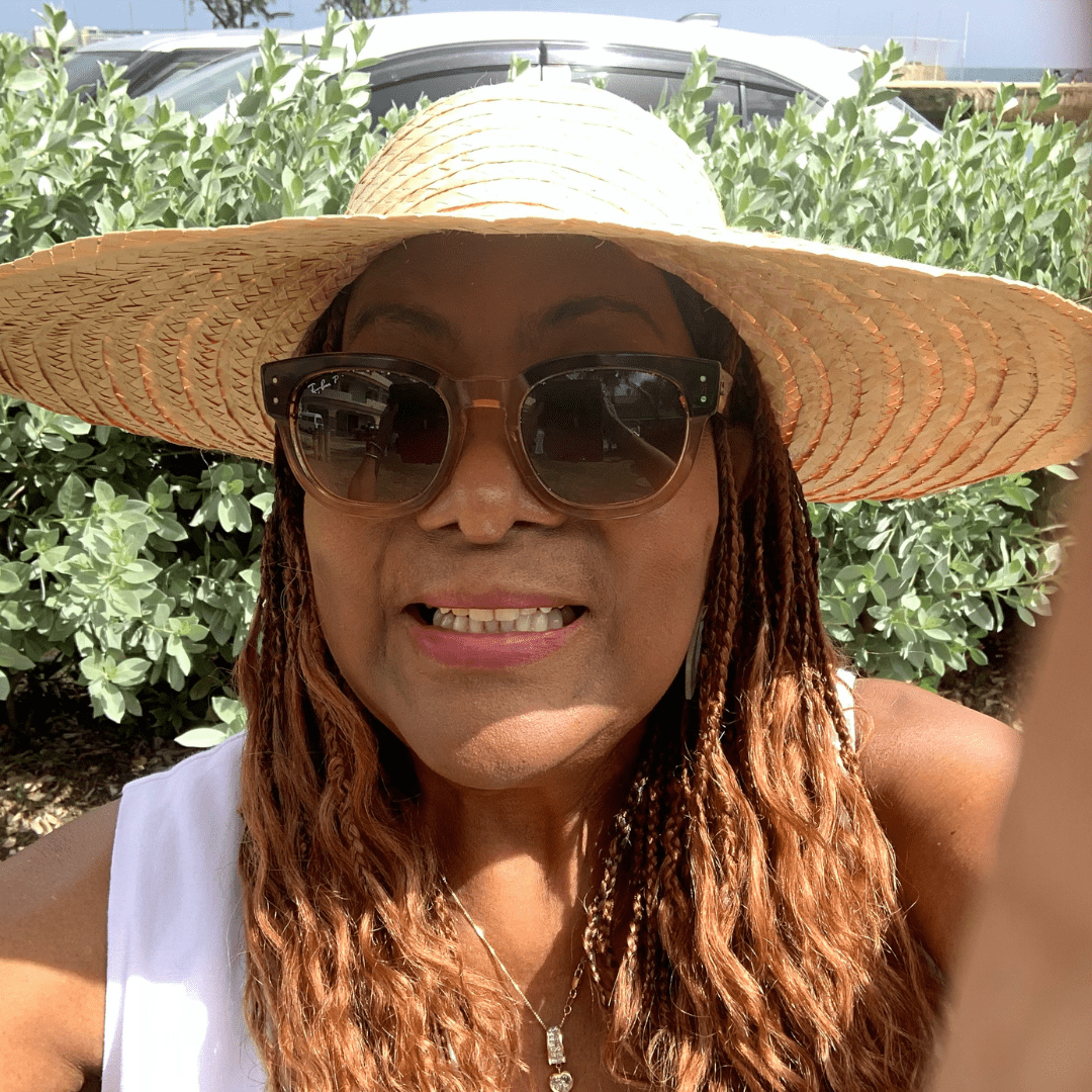 Photo of Leigh Battle enjoying a recent vacation to Barbados with a wide-brimmed hat and sunglasses on her head for sun protection.